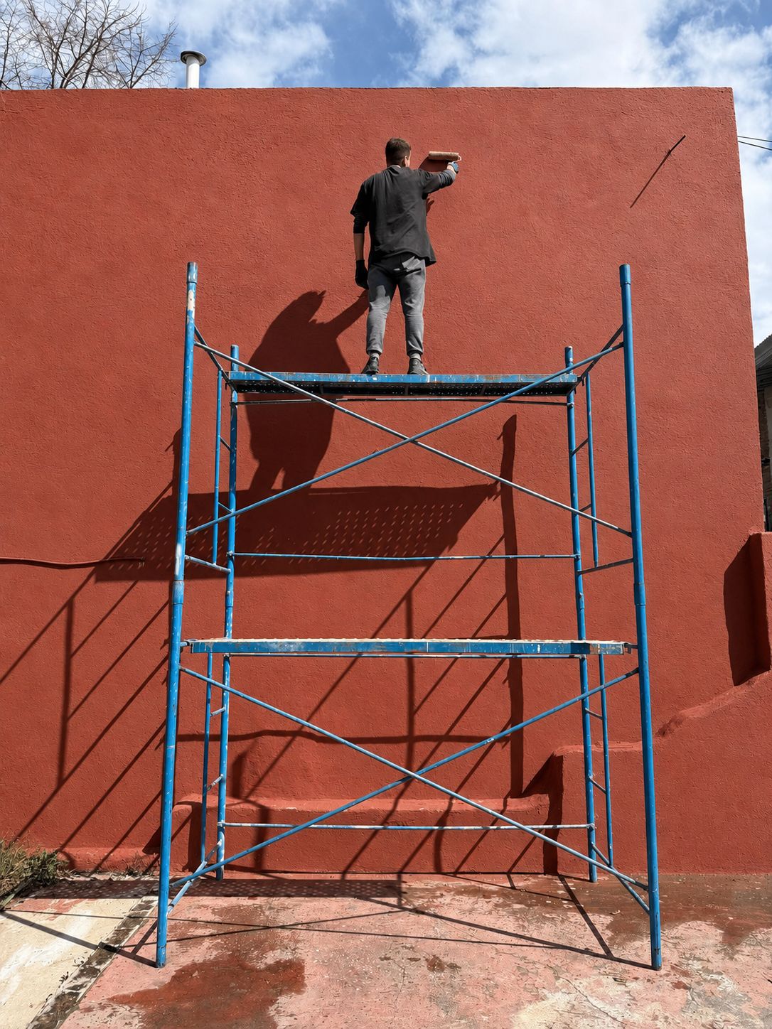 Operario pintando una pared en altura sobre un andamio tubular armado